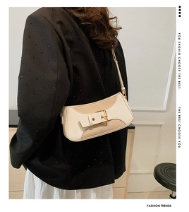 Detail of minimalist leather shoulder bag featuring beige patchwork and gold buckle