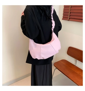 Sac hobo demi-lune rose avec bandoulière plissée porté sur une tenue blazer noir