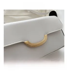 Detail view of smooth white PU leather and golden semi-circular metal hardware on shoulder bag