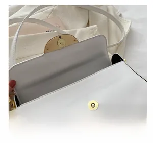 Detail view of the white crossbody bag featuring a golden magnetic buckle closure