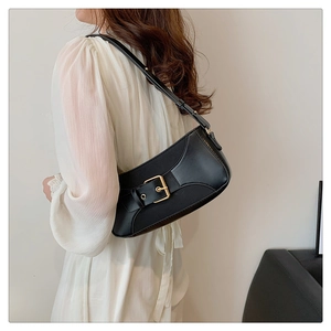 Detail of a black leather crescent shoulder bag with golden buckle on a white dress