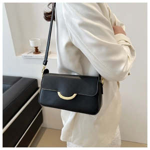 Detail of minimalist black leather shoulder bag with gold hardware clasp on white blazer
