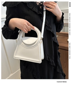 Detail view of a white leather handbag featuring a unique circular integrated handle and strap