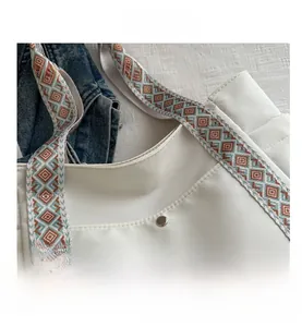 Close-up of a white tote bag featuring a blue and brown geometric jacquard patterned strap