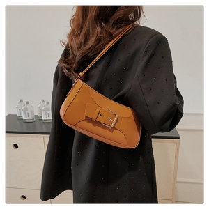 Close-up of a brown leather shoulder bag with a gold buckle worn by a model in a blazer
