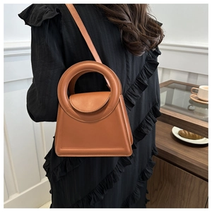Chic camel trapezoidal handbag with large round handle and crossbody strap in a cozy setting