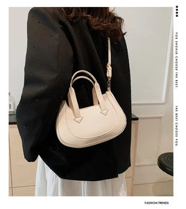 Chic beige leather top-handle bag with adjustable strap worn by a model in a black suit