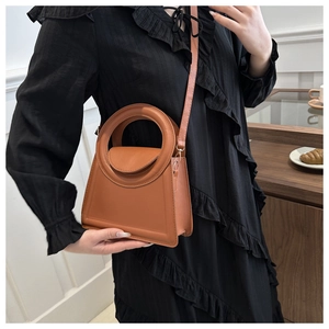Chic tan trapezoid handbag with circular handle shown with black elegant dress