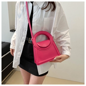 Close-up of fuchsia mini handbag with circular handle and crossbody strap on a model