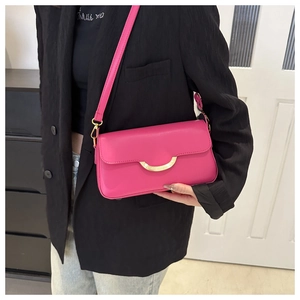 Fuchsia crossbody baguette bag with gold crescent buckle on a black suit blazer