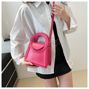 Detail of magenta mini handbag with circular handle and detachable shoulder strap worn by model