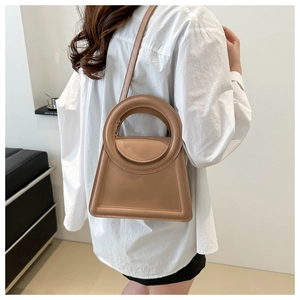 Detailed side view of a camel trapezoid leather handbag with a unique circular handle