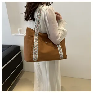 Brown canvas tote bag with geometric ethnic woven strap shown from a side back view