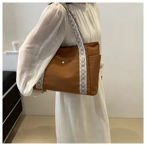 Brown tote bag with geometric tribal pattern strap shown on model's shoulder in casual style