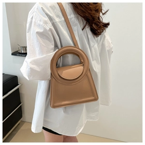 Close-up of khaki leather handbag featuring a unique circular hollow handle and crossbody strap