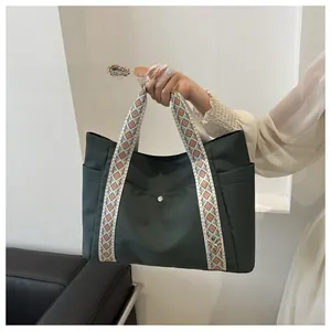 Detail of dark green tote bag featuring woven geometric handles and metal snap pocket