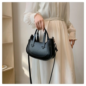Detail of minimalist black leather crossbody bag with curved base on white dress