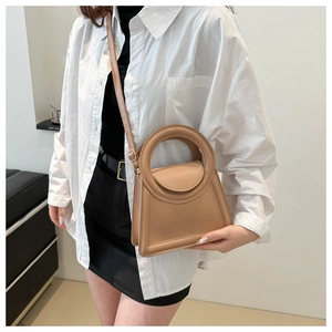 Detail of camel brown trapezoidal handbag with unique circular integrated handle design