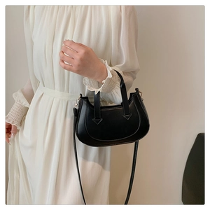 Close-up of a crescent-shaped black leather shoulder bag with fine stitching on a model