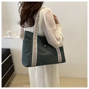 Detail of dark green tote bag with decorative geometric jacquard strap worn by a model