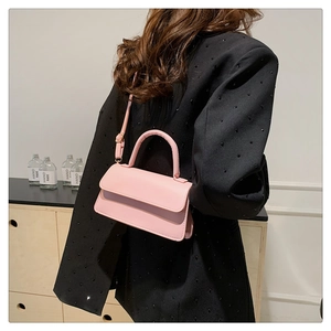 Detail of pink faux leather small shoulder bag styled with a black suit in a home setting