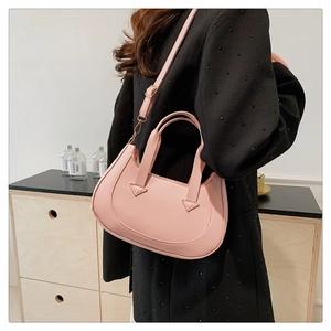Pink crescent leather handbag with triangular stitching worn on the shoulder by a model