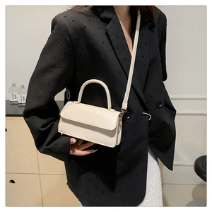 Detail of off-white PU leather bag with top handle and strap shown on a black suit blazer