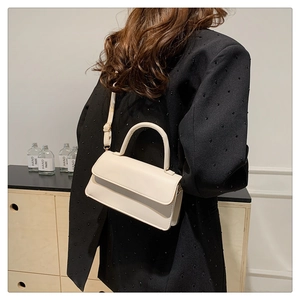 Close-up of cream faux leather shoulder bag worn by model, showcasing size and sleek design