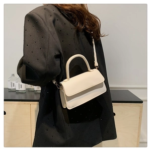 Detail of a creamy white mini shoulder bag with gold hardware and smooth faux leather finish