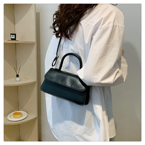 Detail of a minimalist black flap handbag with round handle and adjustable shoulder strap