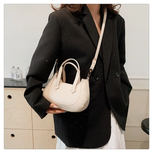 Beige crescent handbag worn with a black blazer showing its elegant crossbody style