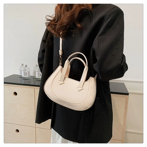 Detail of cream crescent leather handbag with shoulder strap worn by a model in black blazer