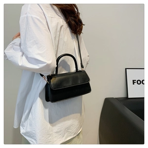Detail view of a black minimalist rectangular shoulder bag with elegant gold metal buckles
