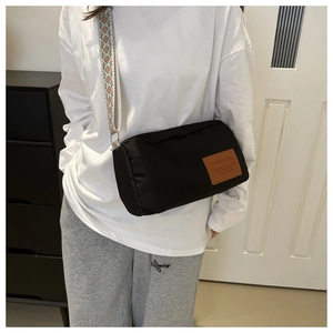 Close-up of black crossbody bag featuring a geometric woven strap and leather label detail