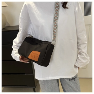 Detail of a black nylon crossbody bag with ethnic geometric woven strap and leather logo
