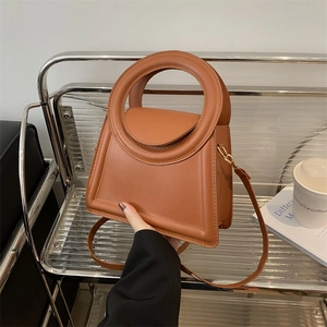 Caramel brown handbag with round cutout handle and crossbody strap in a city lifestyle setting