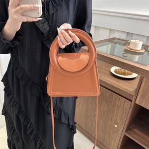 Brown orange minimalist handbag with round handle and crossbody strap in a warm setting