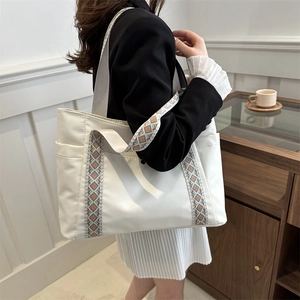Minimalist white nylon tote bag with ethnic pattern strap shown on a female model