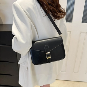 Minimalist black square crossbody bag with gold buckle on a model wearing an ivory blazer