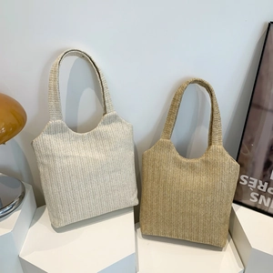Woven tote bags in beige and khaki straw with herringbone pattern on minimalist display
