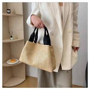 Detail view of woven straw tote bag with black fabric handles in a minimalist lifestyle setting