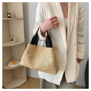 Close-up of woven straw tote bag with black canvas handles shown in a lifestyle setting