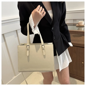 Detail of minimalist cream tote bag showing silver buckle and leather texture on a shoulder strap