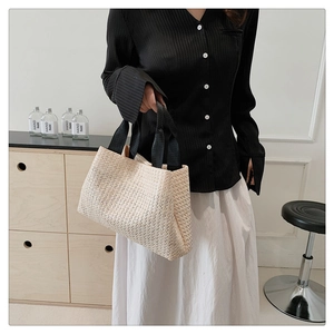 Close-up of beige woven straw tote bag with black handles held by a model