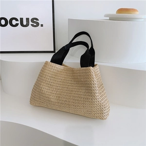 Detailed close-up of handmade woven straw tote bag with black contrast fabric handles