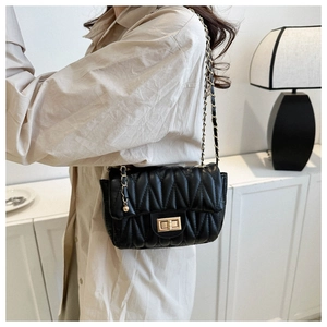 Detail of black quilted saddle bag with gold metal clasp and chain strap on model