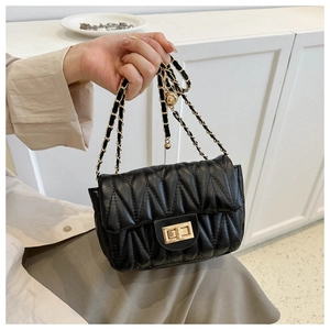Detail of black quilted saddle bag with gold chain strap and metal turn-lock closure