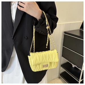 Close-up of bright yellow quilted saddle bag with gold ball chain and twist lock