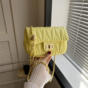 Detail of light yellow quilted saddle bag featuring gold chain and metal ball adjuster