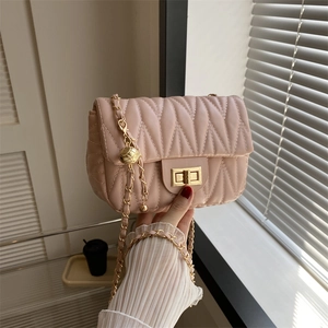 Detail of light pink quilted handbag featuring golden chain strap and hollow ball pendant